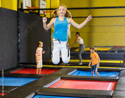 Smiling carefree teenage girl having fun during free-jumping session in indoor trampoline arena..