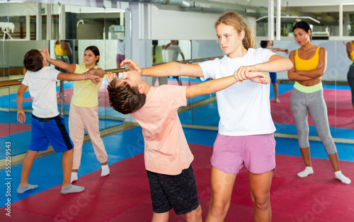 Positive teenager kids in pair exercising self-defense movements during group class