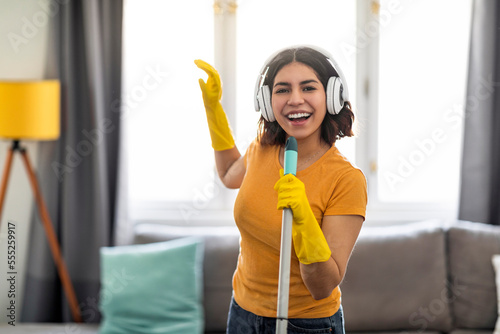 Cheerful Arab Female In Wireless Headphones Singing While Making Cleaning At Home
