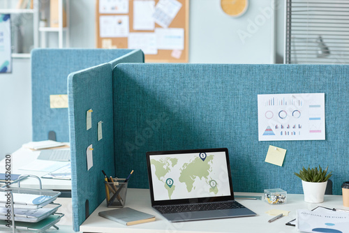 Background image of office cubicle with laptop on desk and world map graphs, copy space