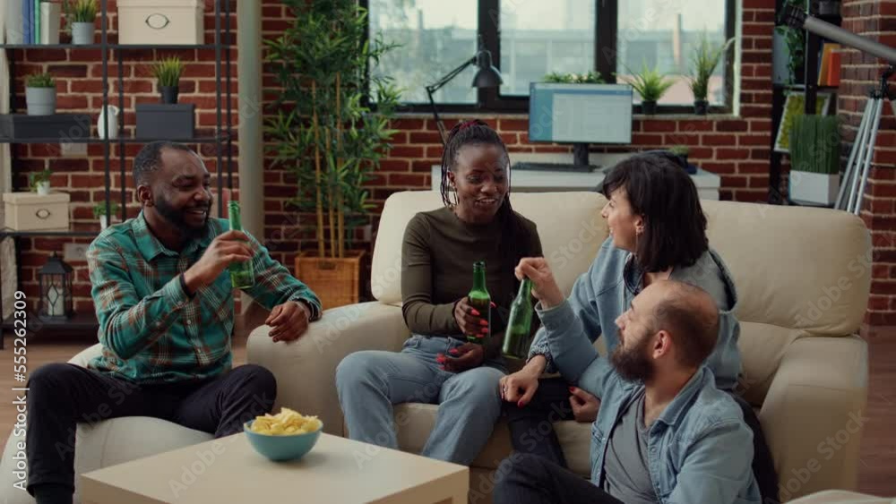 Diverse group of friends clinking bottles of beer to make toast at social gathering, saying cheers. Enjoying conversation and alcohol, talking about happy memories and having fun.