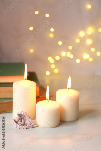 Cute sleeping angel  books and candles on table close up  blurred abstract background. Religious church holiday. symbol of faith in God  Christianity Feast. Romantic relaxation composition