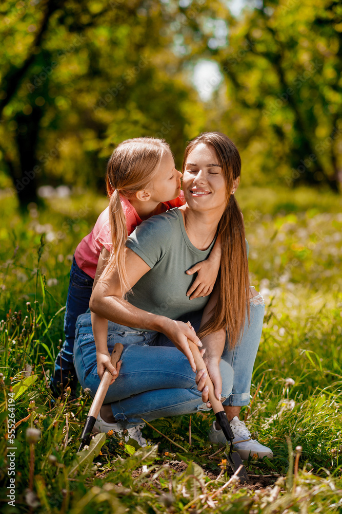 Fototapeta premium Cute woman and a blonde girl spending time in the garden and doing planting