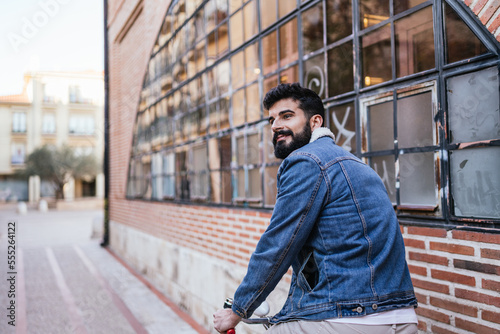 Young man in denim jacket sitting on top of his vintage classic bicycle looking to the side.