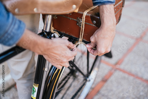 Hands of a young person tying a knot to his carrying case for his vintage classic bicycle.