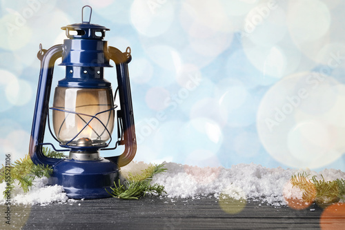 Lantern, snow and fir tree branches on wooden table against blurred lights. Christmas celebration