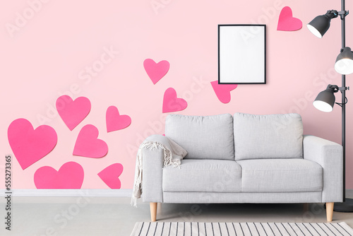 Grey sofa with lamp near pink wall with printed hearts in room