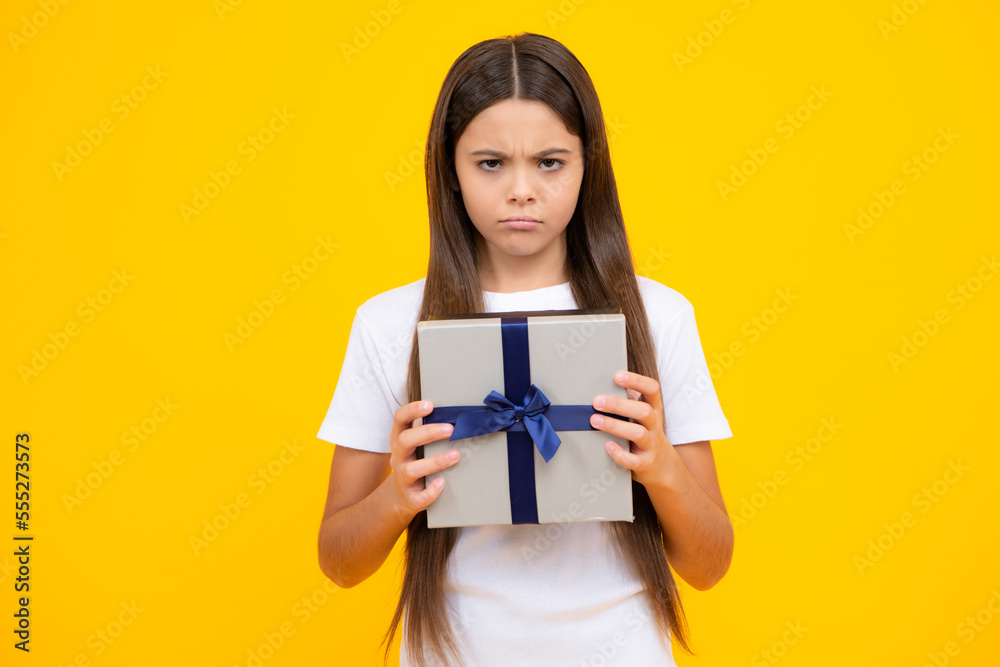 Child with gift present box on isolated studio background. Gifting for kids birthday. Angry face, upset emotions of teenager girl. Child with gift present box on isolated studio background. Gifting for kids birthday. Angry face, upset emotions of teenager girl.