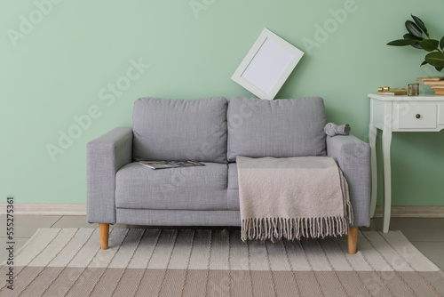 Interior of messy living room with grey sofa, blank frame and table