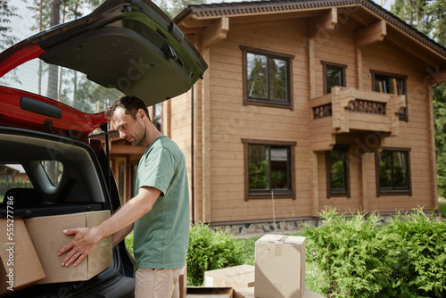 Valokuva Side view portrait of young man unloading boxes from car trunk while moving into