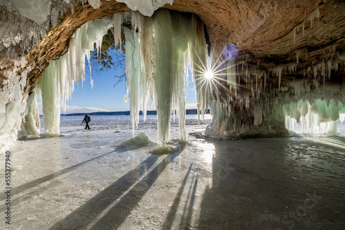 The rising sun shines into an ice cave on Lake Superior. A man trekking across the ice shows the scale of how large it is