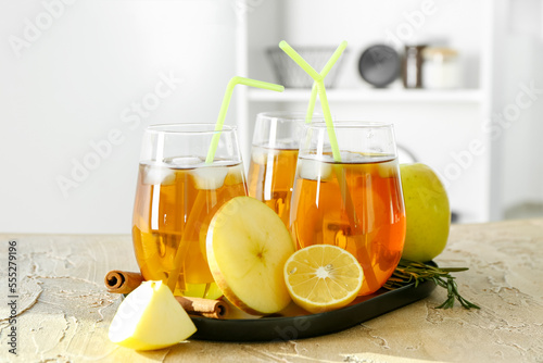 Board with glasses of cold apple juice on table in kitchen