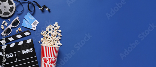 Flat lay composition with clapperboard, cinema tickets and popcorn on blue background, space for text. Banner design