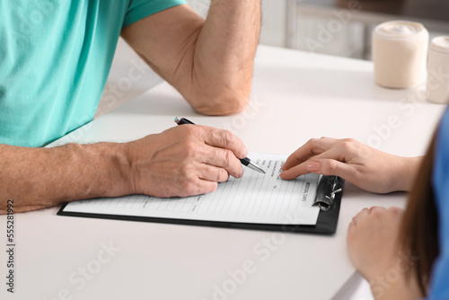 Doctor helping patient filling his medical card at table in clinic, closeup