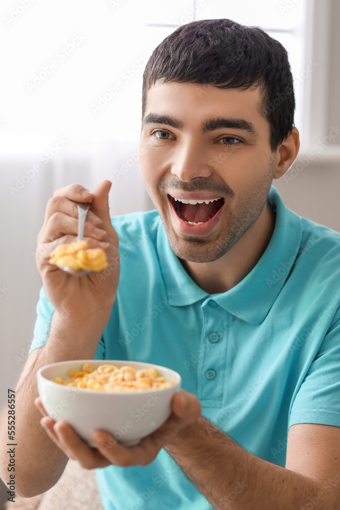 Happy young man eating cornflakes with spoon at home, closeup Happy young man eating cornflakes with spoon at home, closeup