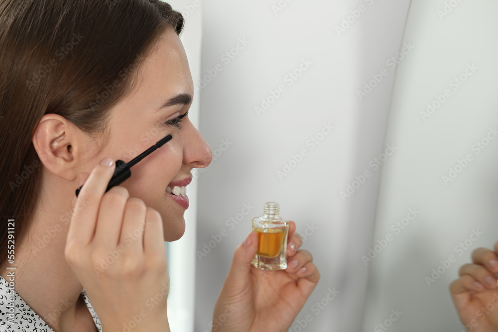 Fototapeta premium Young woman applying oil on her eyelashes indoors