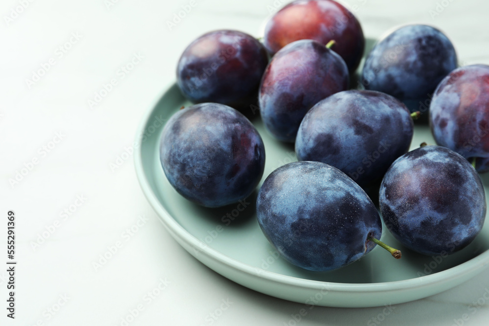 Plate with tasty ripe plums on white table, closeup