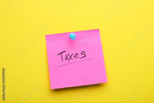 Paper note with word Taxes pinned on yellow background