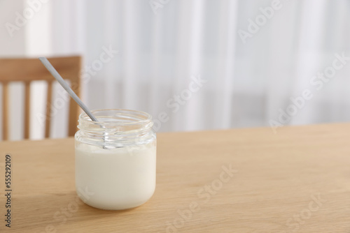 Jar of delicious yogurt with spoon on wooden table indoors. Space for text