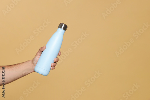Man holding thermo bottle on beige background, closeup. Space for text