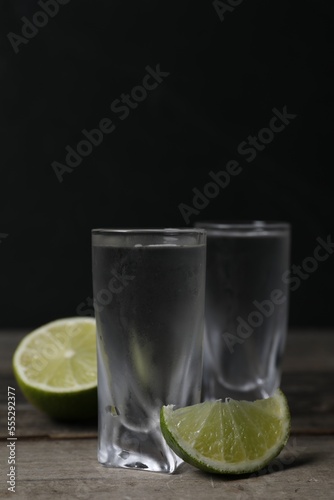 Shot glasses of vodka with lime on wooden table. Space for text