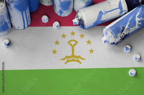 Tajikistan flag and few used aerosol spray cans for graffiti painting. Street art culture concept, vandalism problems photo
