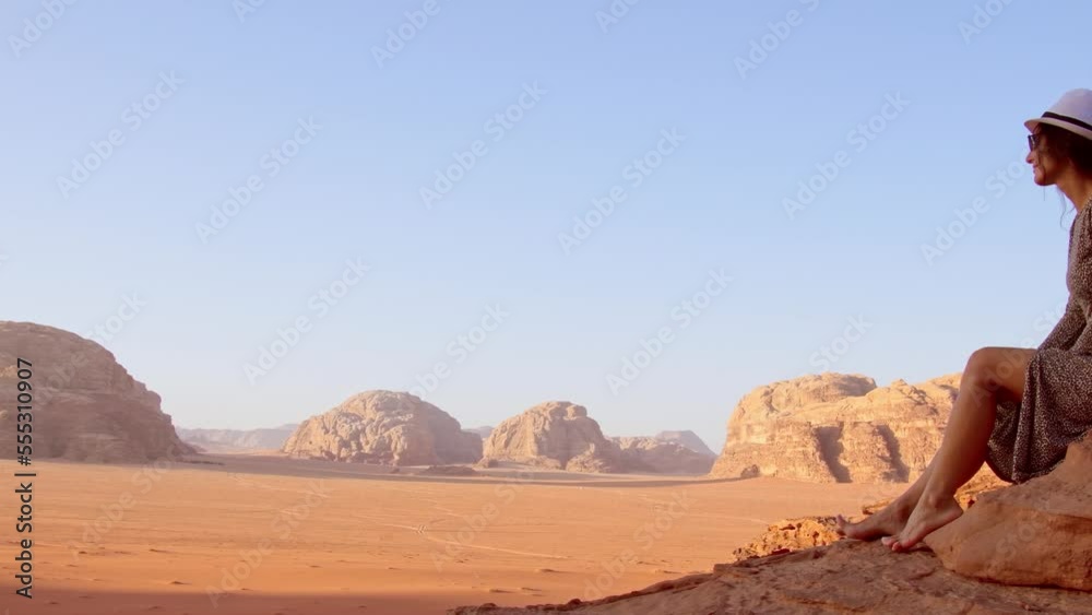 Woman tourist in dress sit on cliff barefoot at viewpoint on sunrise in Wadi Rum desert - valley Wadi Saabit. Jordan explore concept Woman tourist in dress sit on cliff barefoot at viewpoint on sunrise in Wadi Rum desert - valley Wadi Saabit. Jordan explore concept