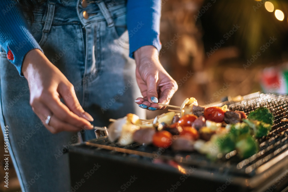 Close up hand of Woman cooking meat on barbecue grill at new year party. Bar-B-Q or BBQ on traditional stove. Night Party, people and celebration concept.