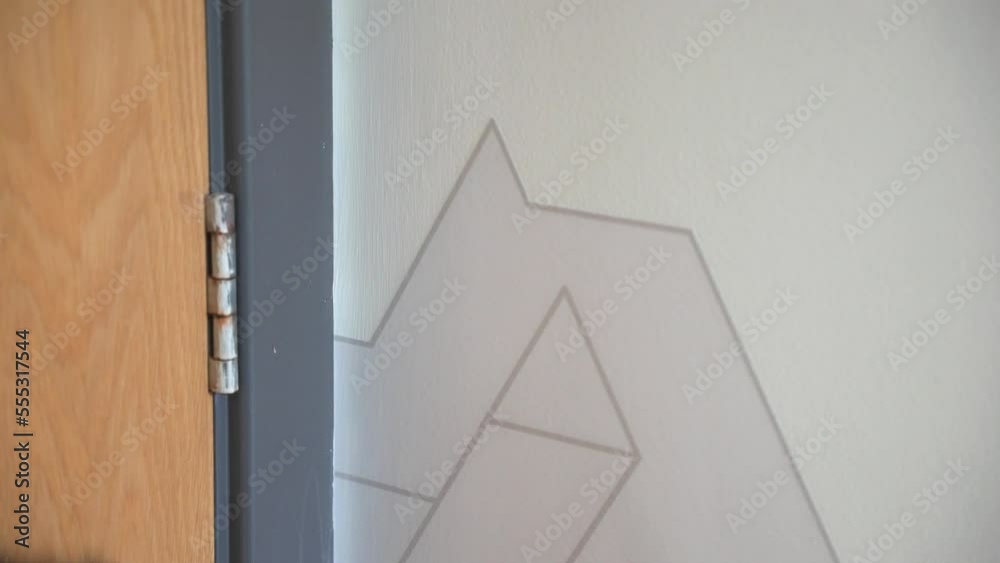 Workman installing vinyl wall graphic on to wall for client with geometric design using squeegee applicator in office space