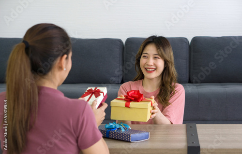 Two Asian women enjoy giving each other gift boxes on a special occasion.