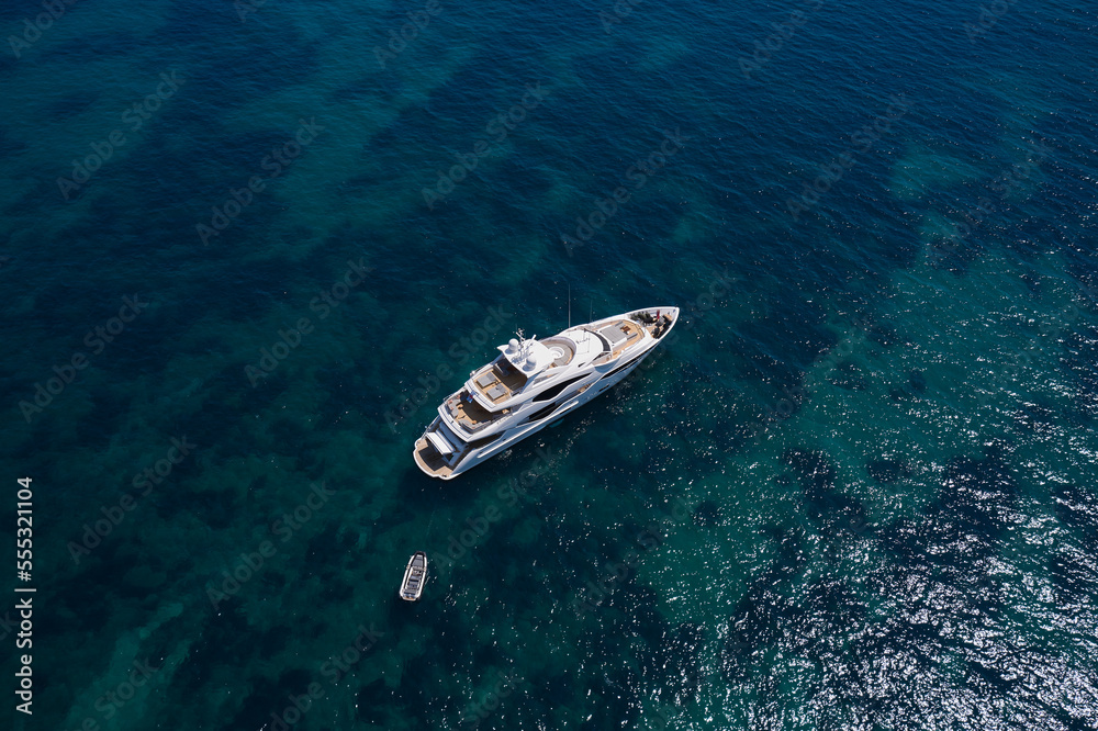 A large white yacht is anchored on clear water, top view. Super yacht in the sea top view. A large white yacht is anchored on clear water, top view. Super yacht in the sea top view.