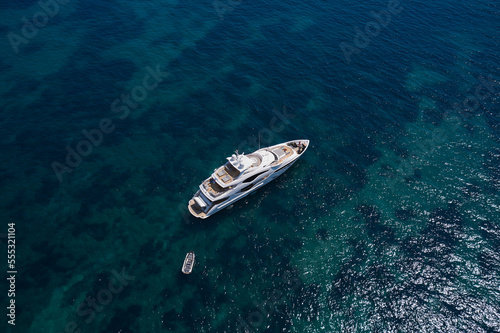 A large white yacht is anchored on clear water, top view. Super yacht in the sea top view.
