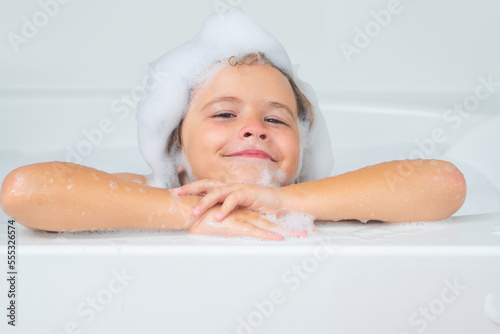 Little child in a bath tub. Washing in bath. Kid with soap suds on hair taking bath. Closeup portrait of smiling kid, health care and kids hygiene. Kids face in bath tub with foam close up. photo