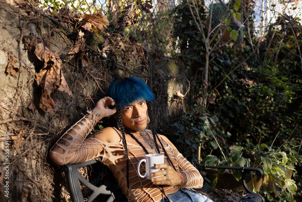 Naklejka premium indigenous non-binary artist drinking tea in urban garden in autumn