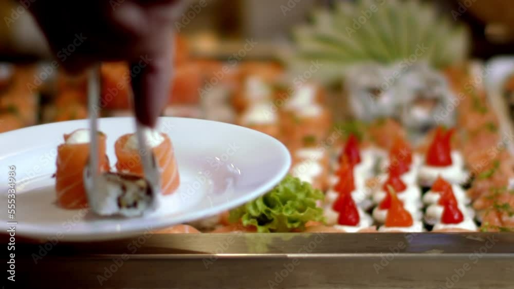 Person choosing salmon sushi roll at an Asian-Japanese buffet Person choosing salmon sushi roll at an Asian-Japanese buffet
