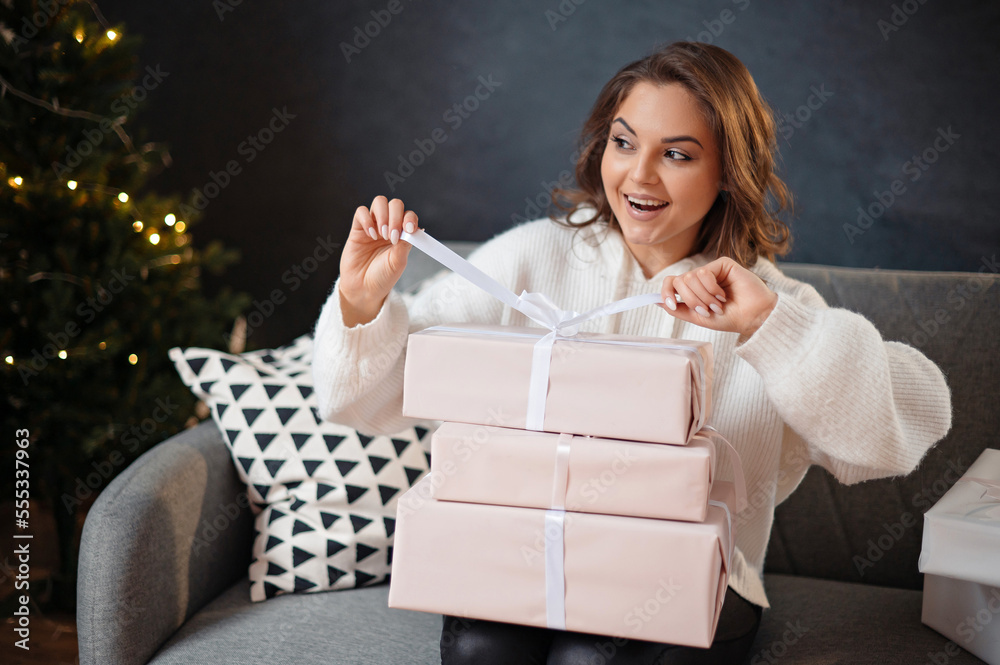 Overjoyed young lady with curly hair tying bow at gift box while sitting at the sofa Overjoyed young lady with curly hair tying bow at gift box while sitting at the sofa