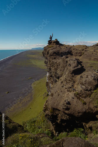 Tourist posing on large rock landscape photo. Beautiful nature scenery photography with black beach on background. Idyllic scene. High quality picture for wallpaper, travel blog, magazine, article