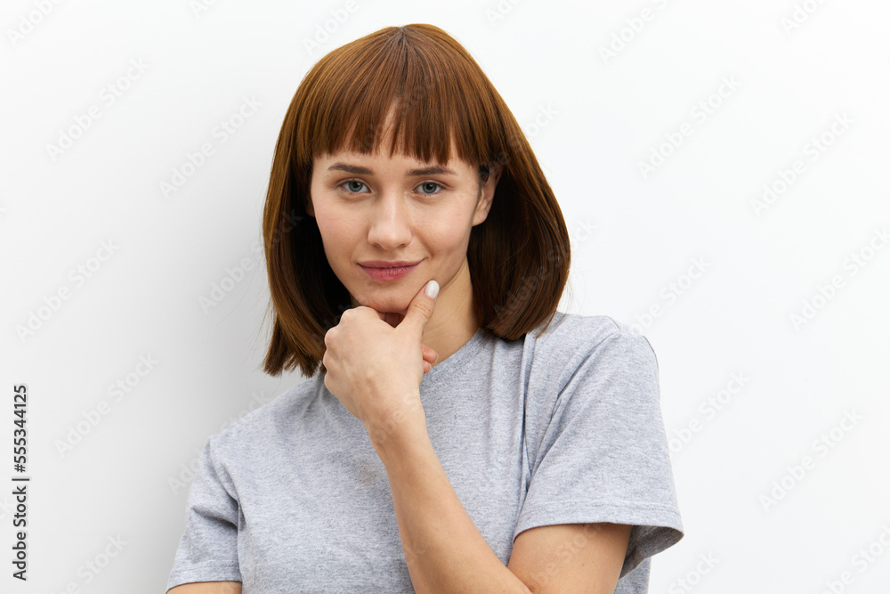 a sweet, thoughtful, beautiful woman stands on a white background in a gray cotton T-shirt and thoughtfully holds her hand near her face a sweet, thoughtful, beautiful woman stands on a white background in a gray cotton T-shirt and thoughtfully holds her hand near her face
