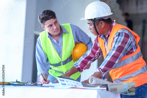 Two construction engineers holding blue print and inspecting the construction site