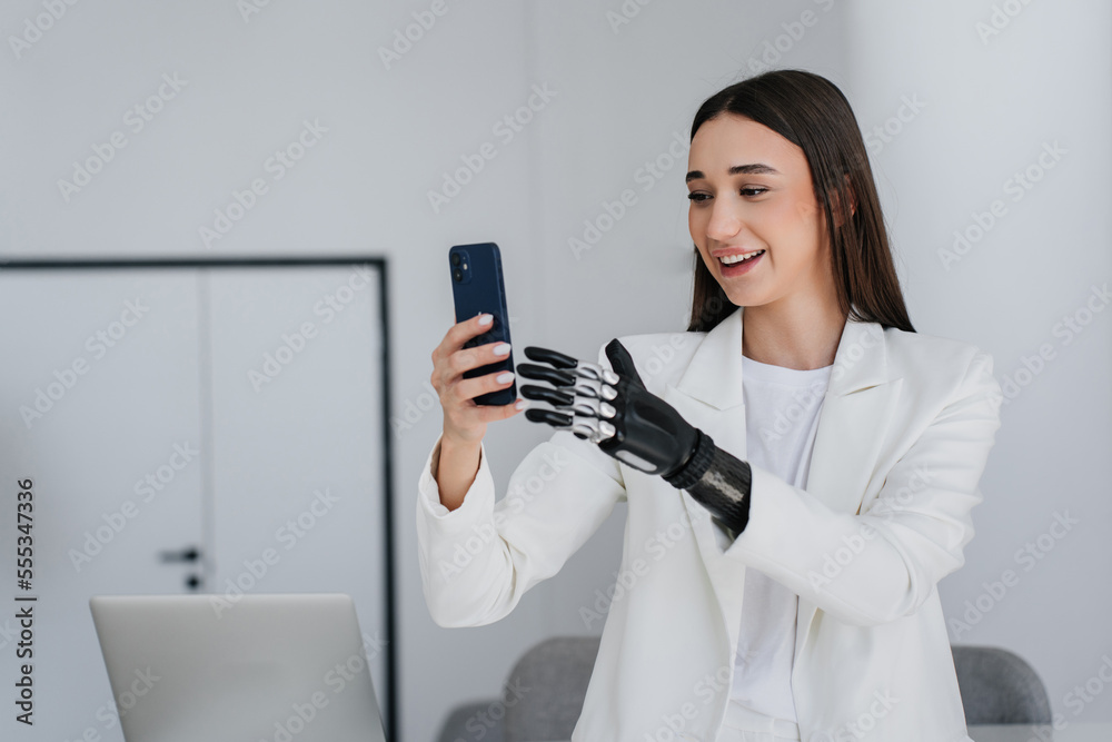 Cheerful gorgeous brunette girl with bionic arm talks by phone, smiles makes video call at home. young woman with artificial hand laughing. Mockup, cyber arm. Medicine. Orthopaedics hi tech. Cheerful gorgeous brunette girl with bionic arm talks by phone, smiles makes video call at home. young woman with artificial hand laughing. Mockup, cyber arm. Medicine. Orthopaedics hi tech.