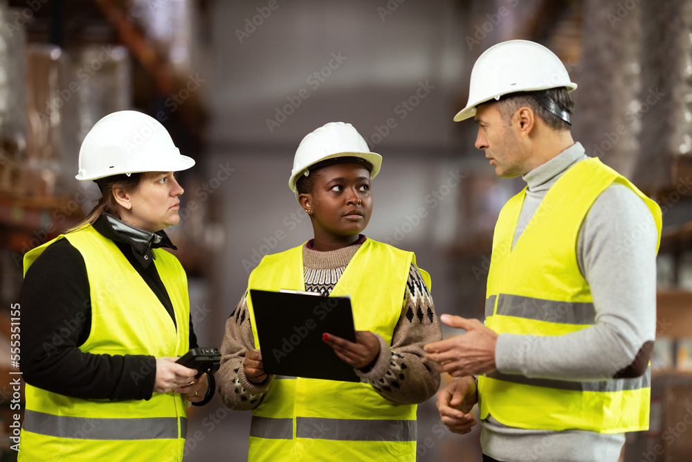 A multiracial group of people is working in a distribution warehouse, the manager is giving instructions to the workers.