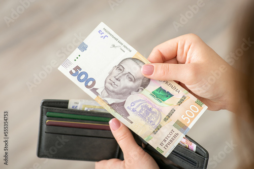 Banknote of 500 hryvnias in female hand close up. Grey wallet with ukrainian money and credit cards on the background