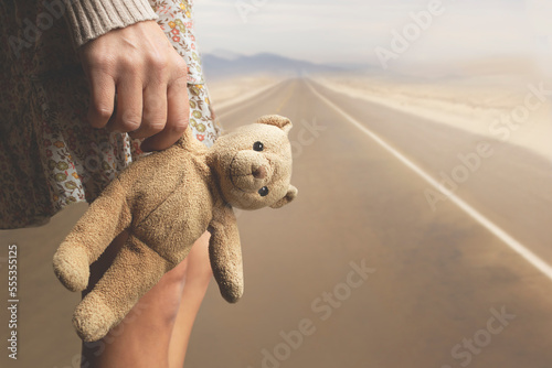 Fototapeta girl holds her teddy bear in hand along a road to abandon it, concept of person'