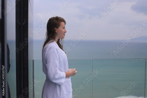 Beautiful woman, young girl in a white bathrobe in a spa, luxury hotel on the rooftop with sea or ocean view, the islands, resting, relaxing and smiling, enjoying vacation 
