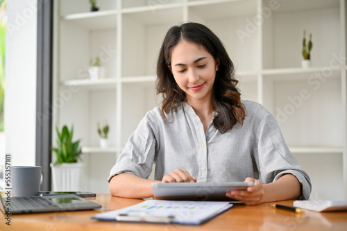 Attractive Asian businesswoman or female manager using digital tablet at her office desk.