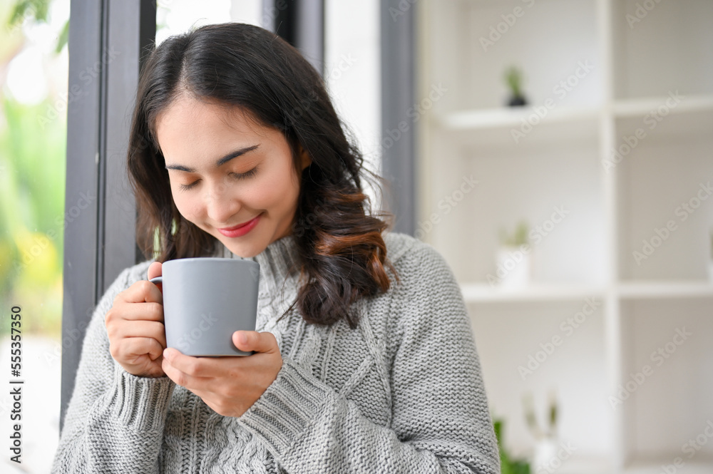Peaceful Asian woman in cozy sweater smelling, enjoying with her morning coffee. Peaceful Asian woman in cozy sweater smelling, enjoying with her morning coffee.