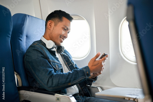 Картината върху платно side view, Asian male passenger using his smartphone during the flight