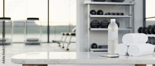 Copy space on white tabletop with a bottle of water  towels over modern fitness center