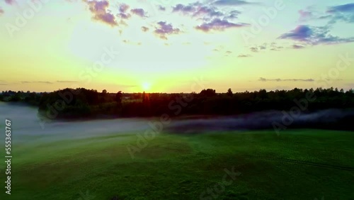 scenic rural landscape shrouded in fog and orange colored sunrise at horizon. Aerial flyback drone view photo