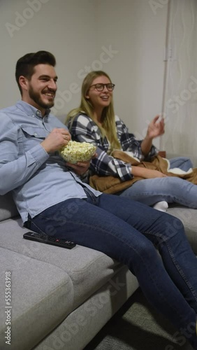 Young couple woman and man sitting at home on sofa eating popcorns and watching movie on television. Married people together enjoy the film while female explaining to male scene and plot of the film.
